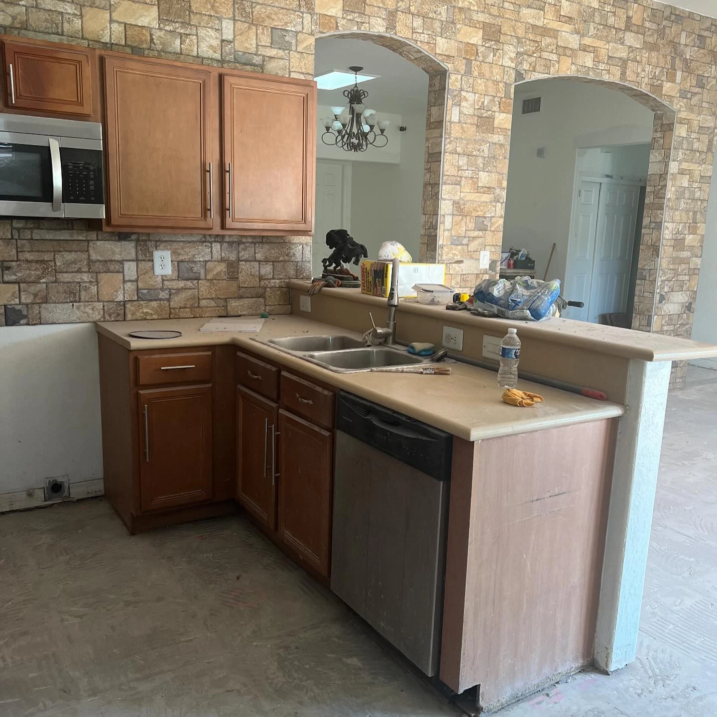 Before: kitchen with brown wood cabinetry, stone wall finishes, and an unfinished floor